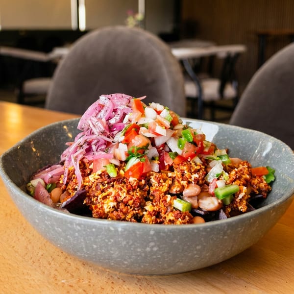 A vibrant bowl of chorizo, pico de gallo, and pickled onions on a wooden table in a restaurant.