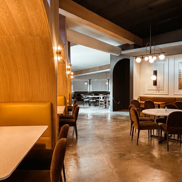 Spacious restaurant interior with curved wooden booths, round tables, and modern light fixtures.