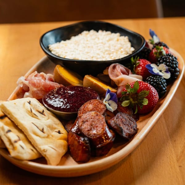 Appetizer board with meats, cheeses, berries, flatbread, and jam, garnished with edible flowers.