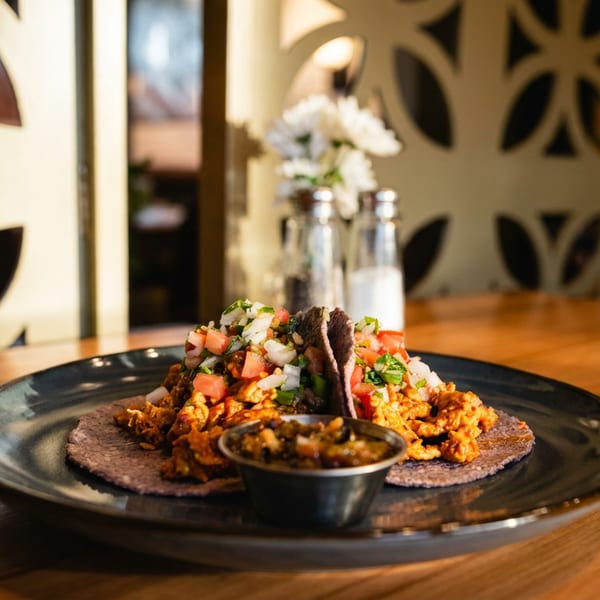 Two breakfast tacos topped with pico de gallo and a side of salsa on a dark plate.